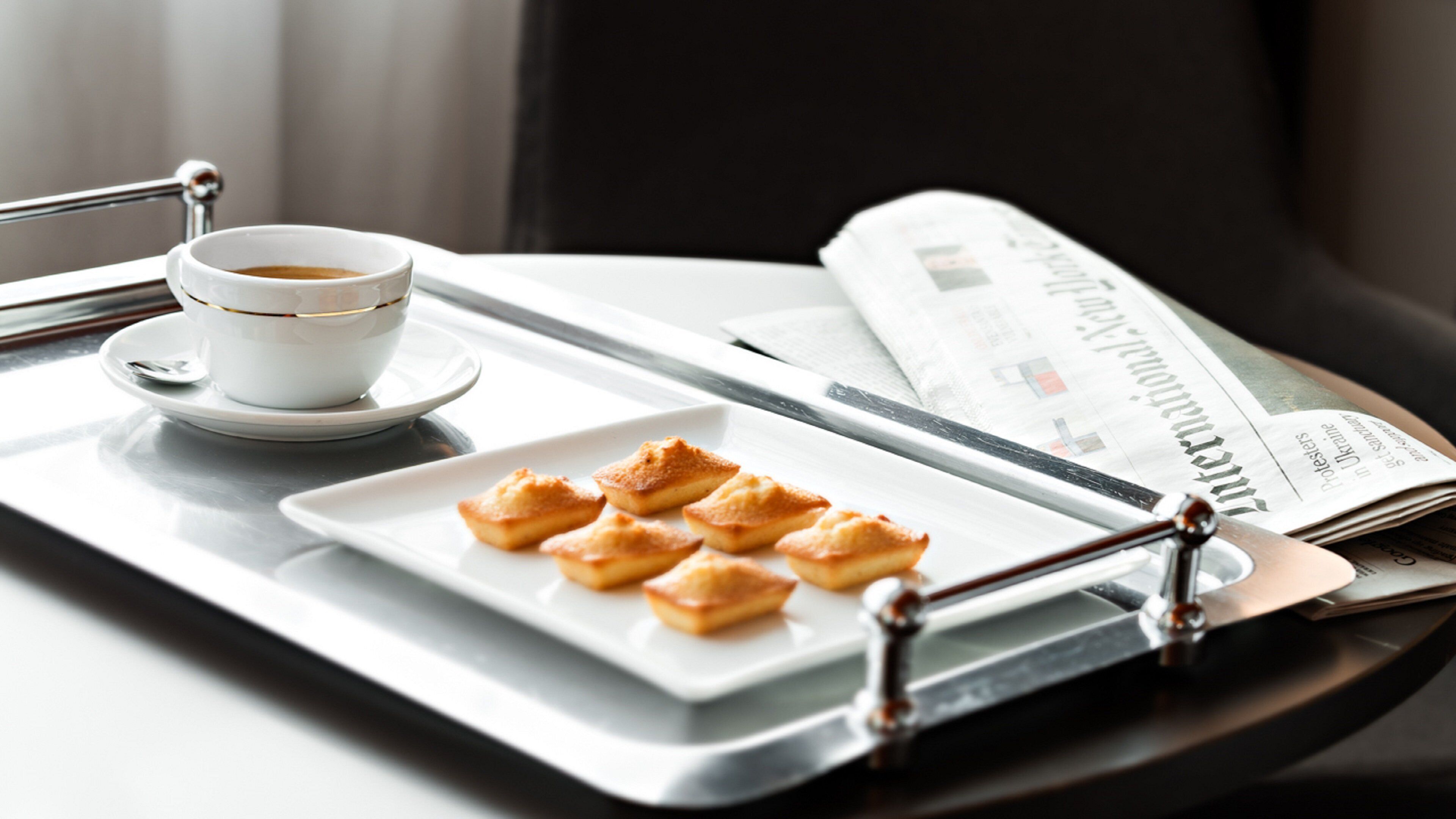 A tray with pastries, a cup of coffee, and a newspaper on a table.