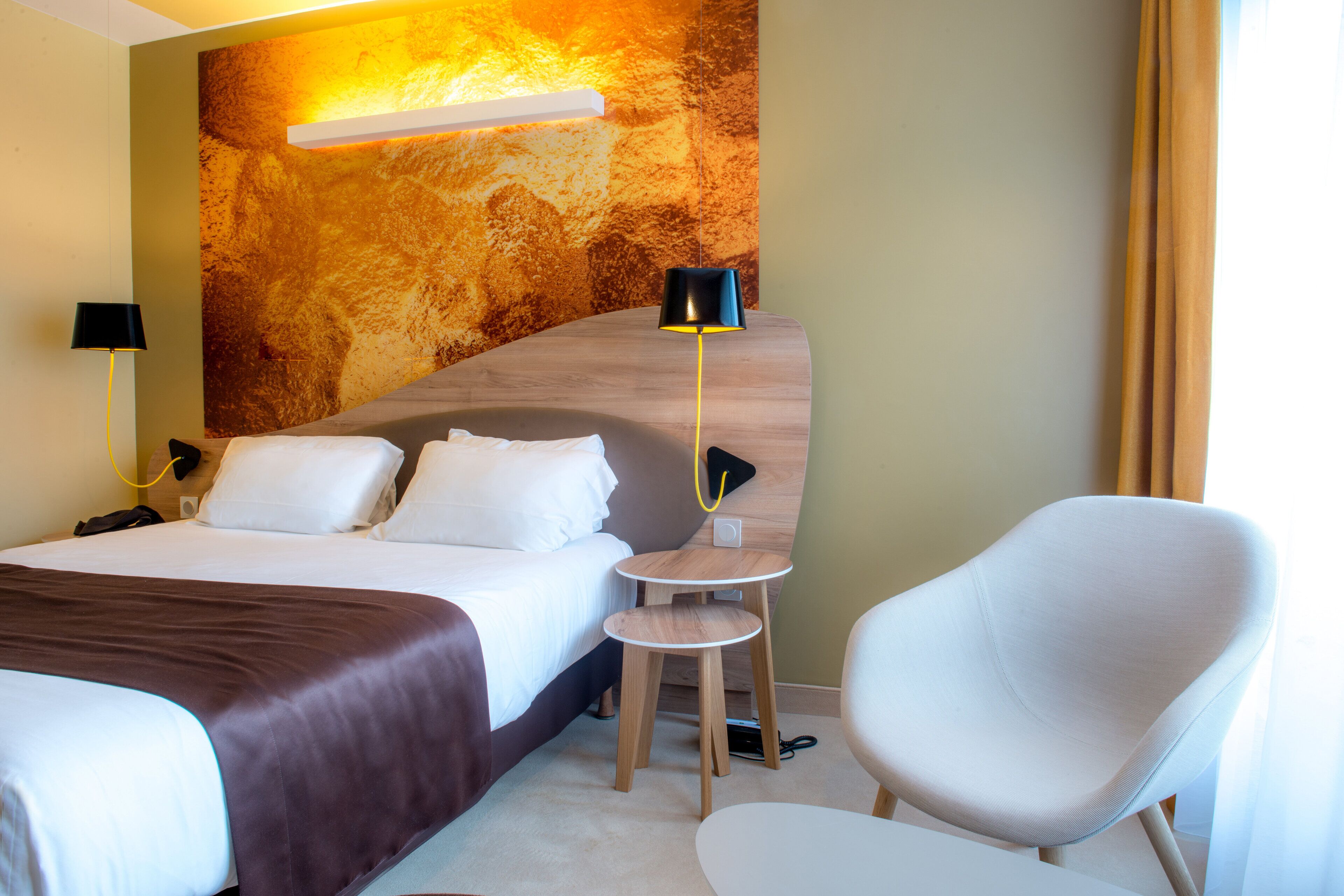 Ein Hotelzimmer mit einem großen Bett, einem Nachttisch, einem Sessel und einer Wandlampe.