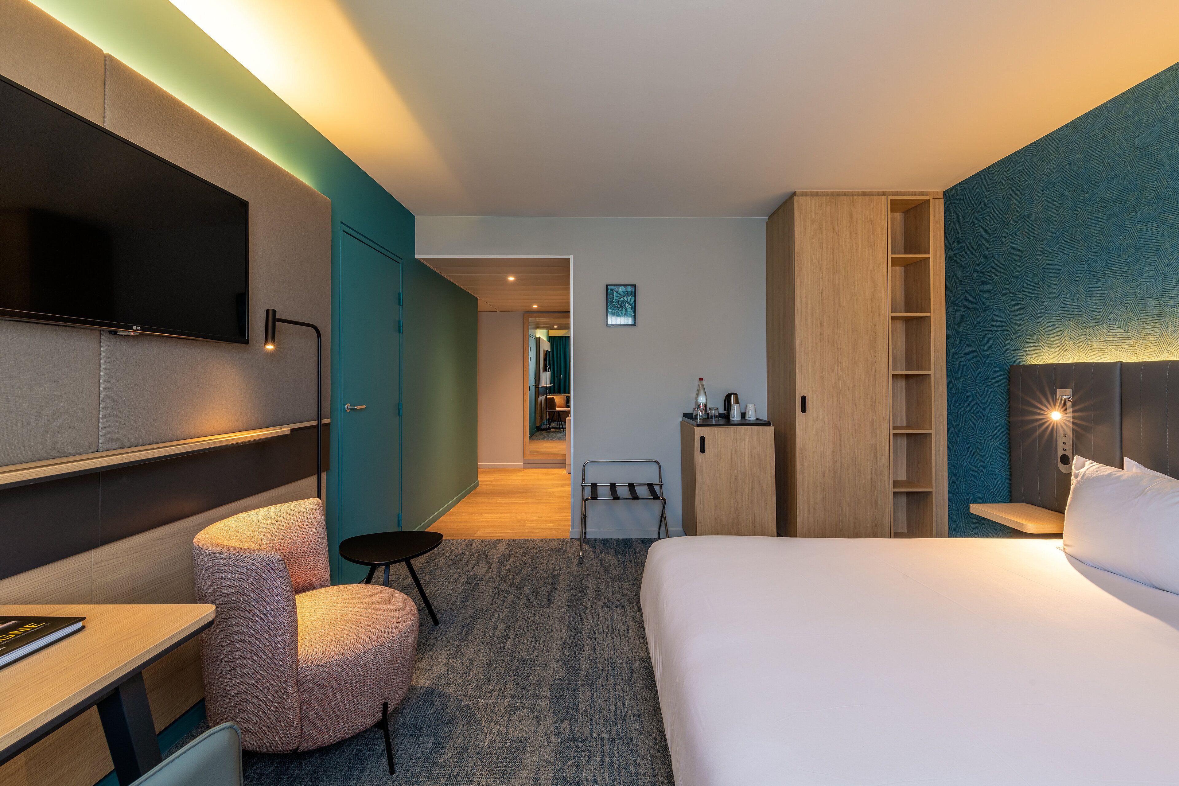 A modern hotel room with a flat-screen TV, a bed, a desk, a chair, and a small table.
