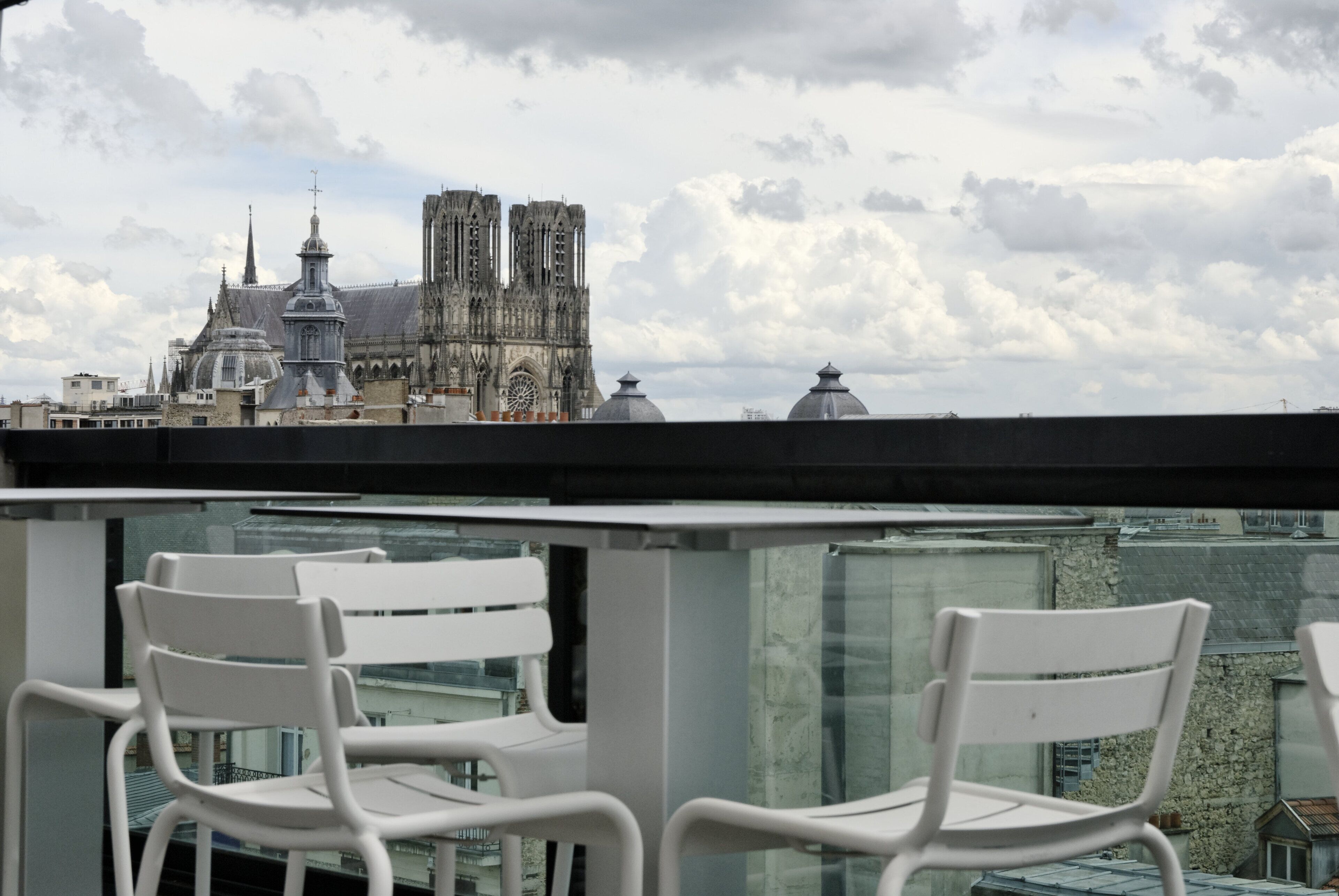 A view of a cathedral with two towers and a dome, seen from a balcony with white chairs.