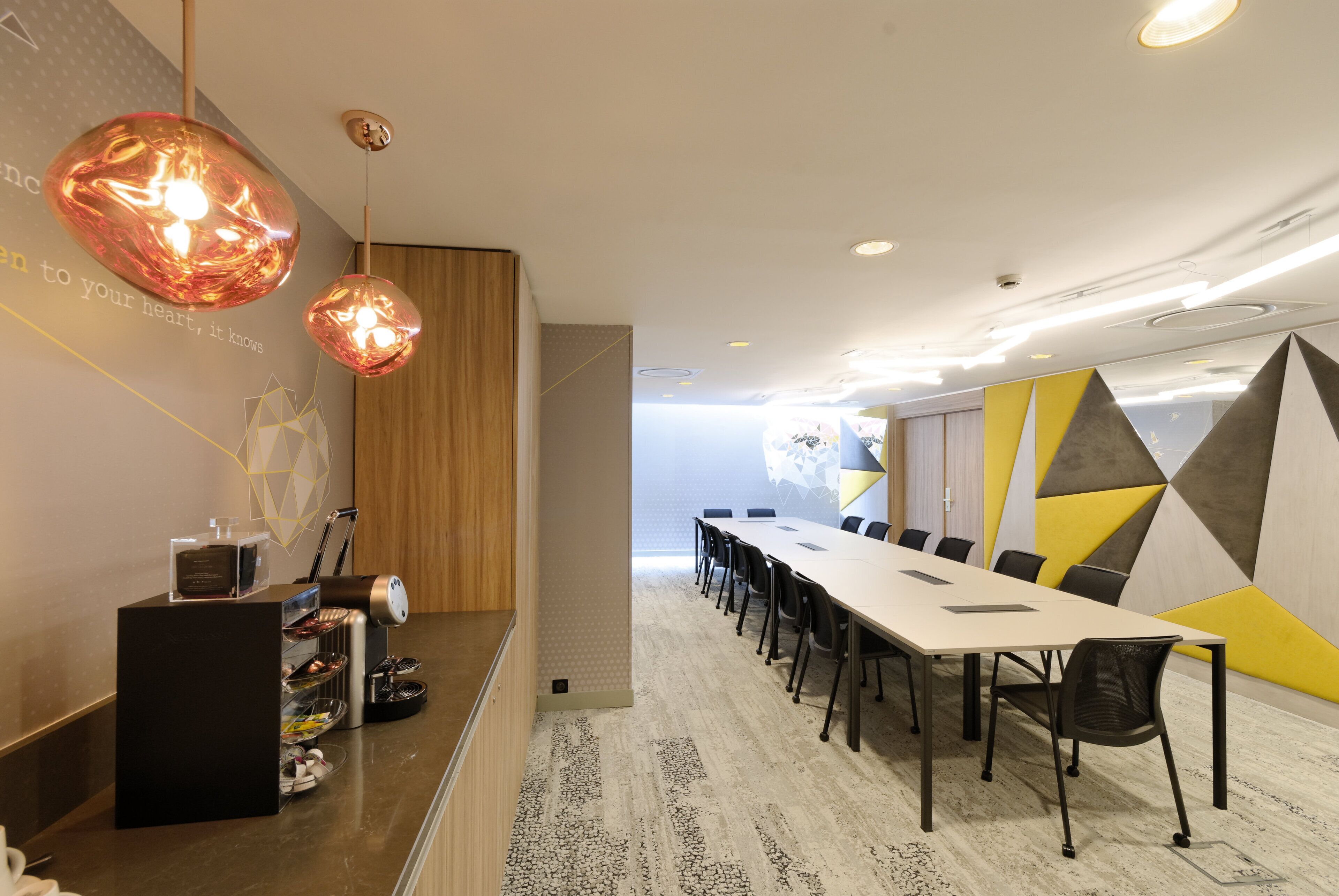 Egy modern konferenciaterem, amelyben egy hosszú asztal, székek és egy recepciós terület található, pulttal és egyéb kényelmi szolgáltatásokkal.