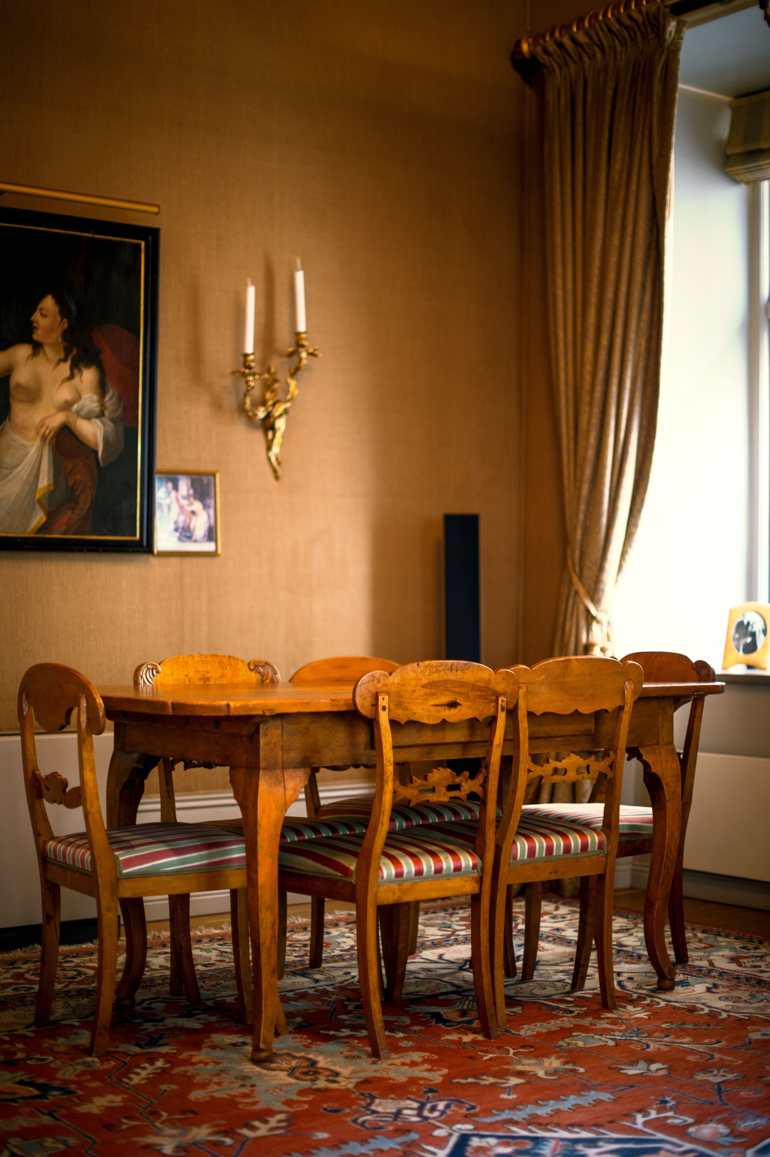Un coin repas avec une table et des chaises en bois, un tapis à motifs, un tableau et un chandelier fixé au mur.