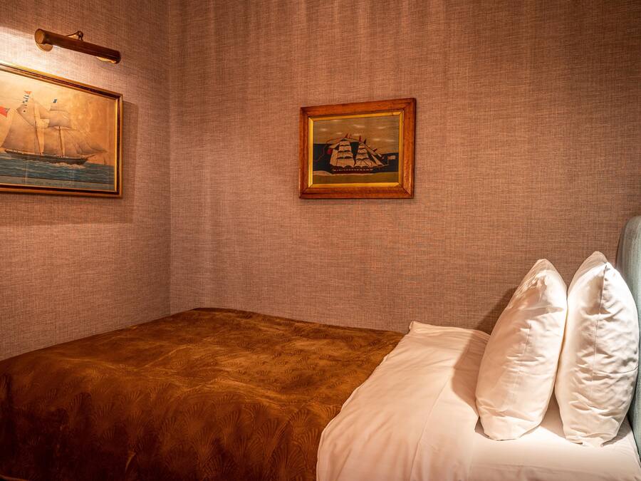 A bedroom with a bed, pillows, and two framed pictures on the wall.