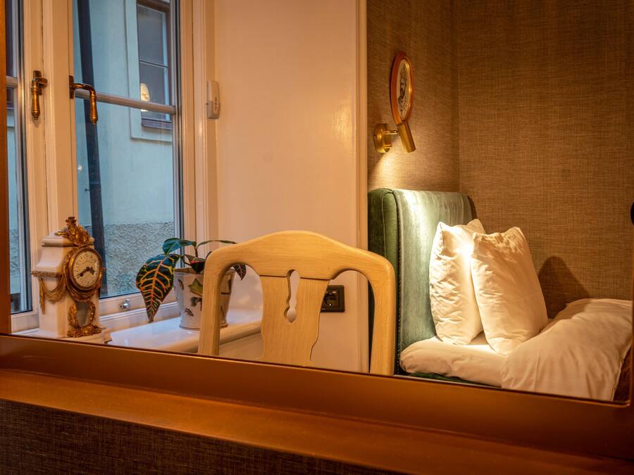 Una habitación de hotel con una cama, una mesita de noche, un espejo, un reloj y una ventana.