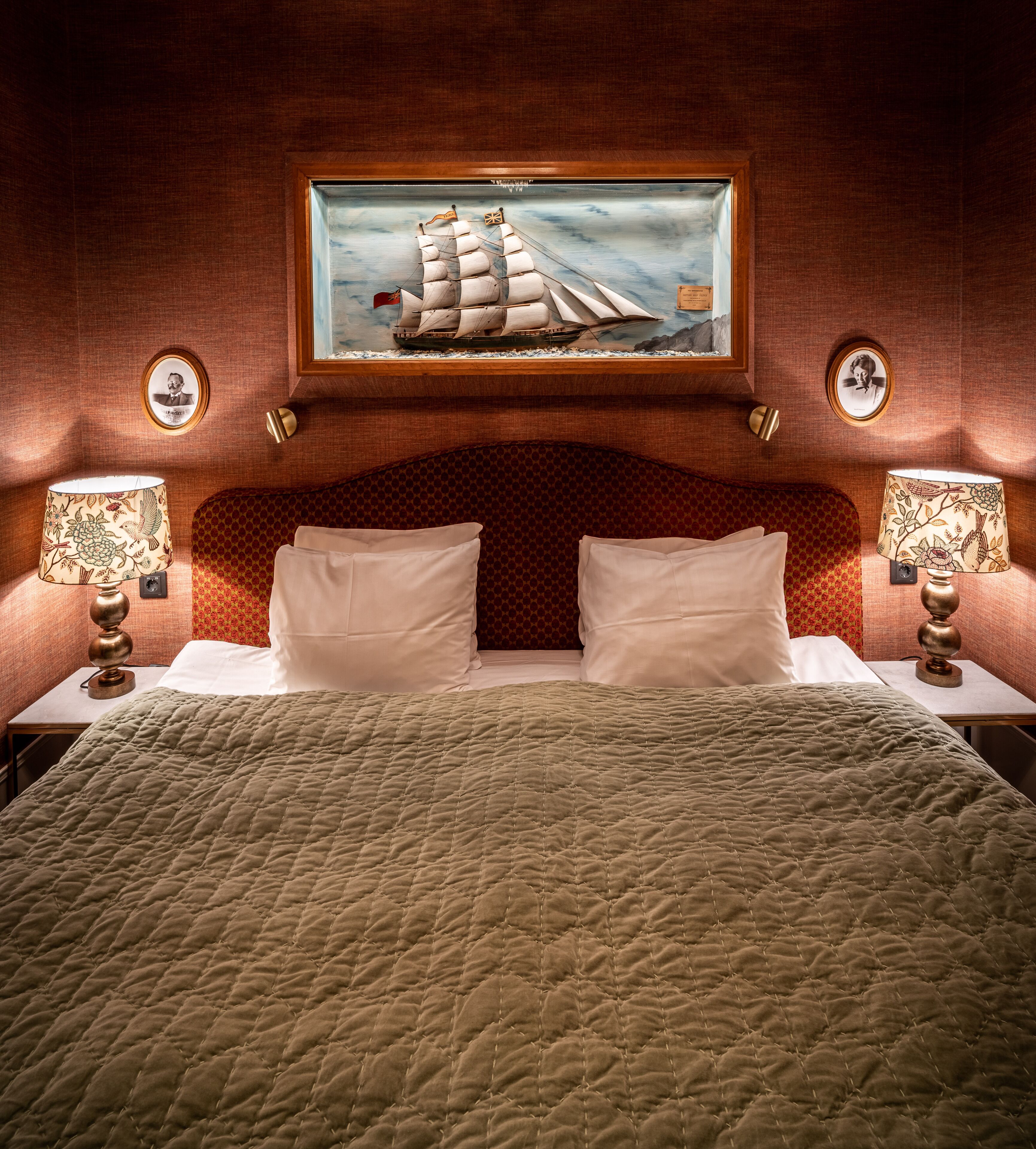 A bed with a quilted cover, two white pillows, and a framed painting of a sailing ship above it.