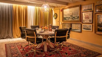Een eetruimte met een ronde tafel, zwarte stoelen, een vloerkleed met een rood patroon, en maritieme kunstwerken aan de muren.