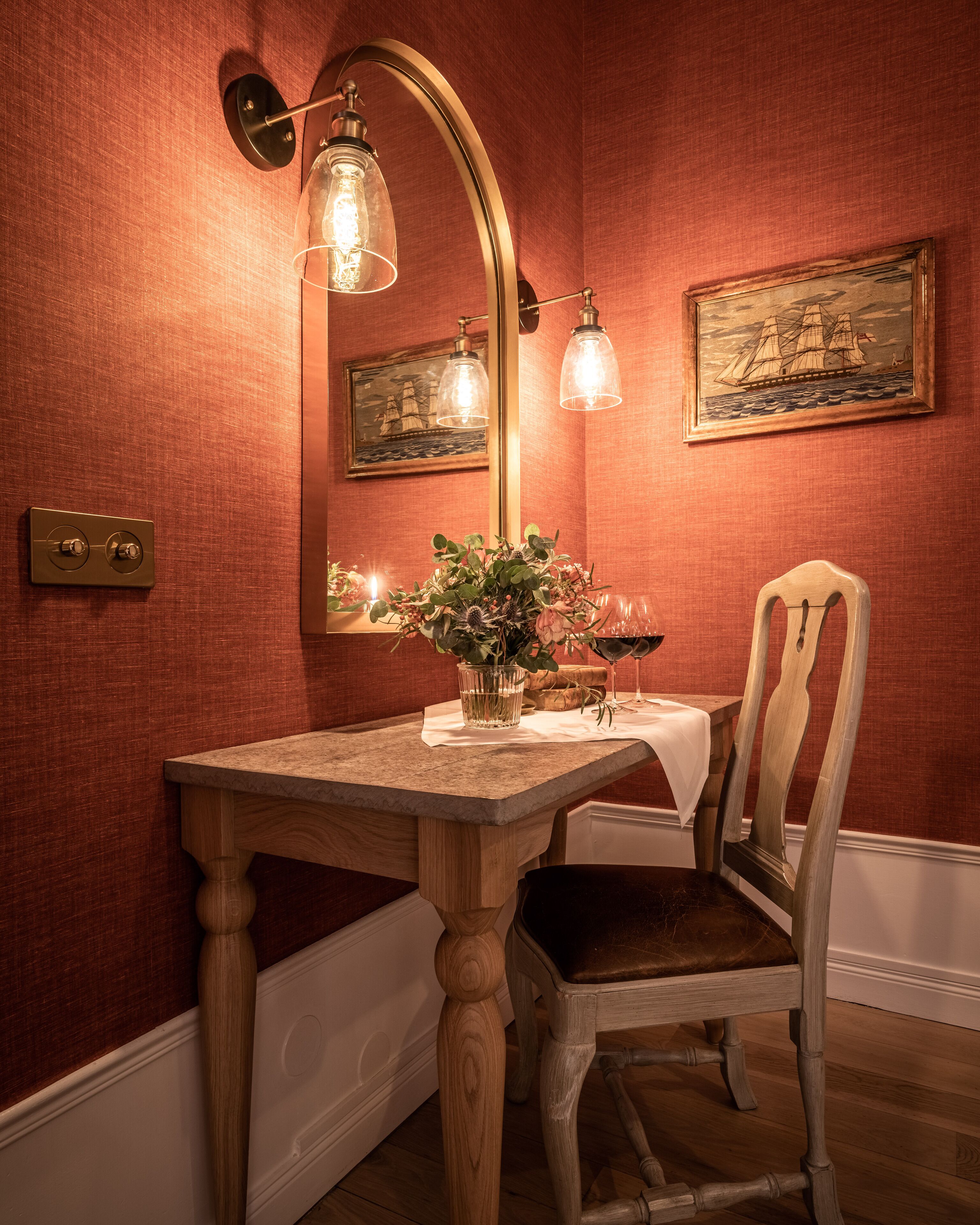 A wooden dining table with a vase of flowers, a candle, and a wine glass. There is a chair and a mirror on the wall.