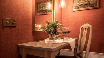 Una mesa de comedor de madera con un florero, una vela y una copa de vino. Hay una silla y un espejo en la pared.