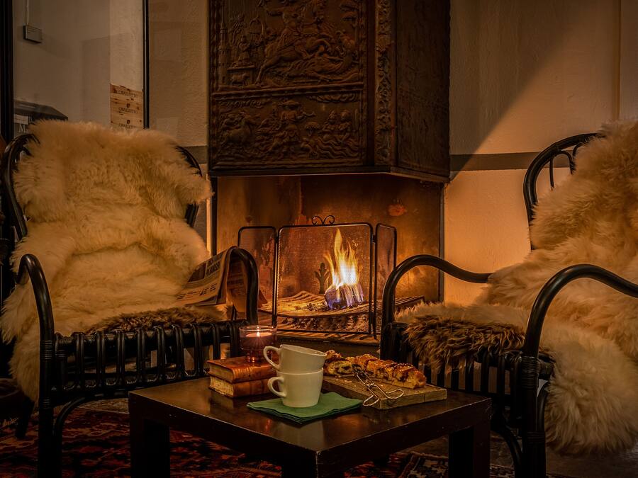 Un ambiente acogedor con chimenea, dos sillones cómodos, una mesita de centro con un libro y una taza, y una alfombra estampada.