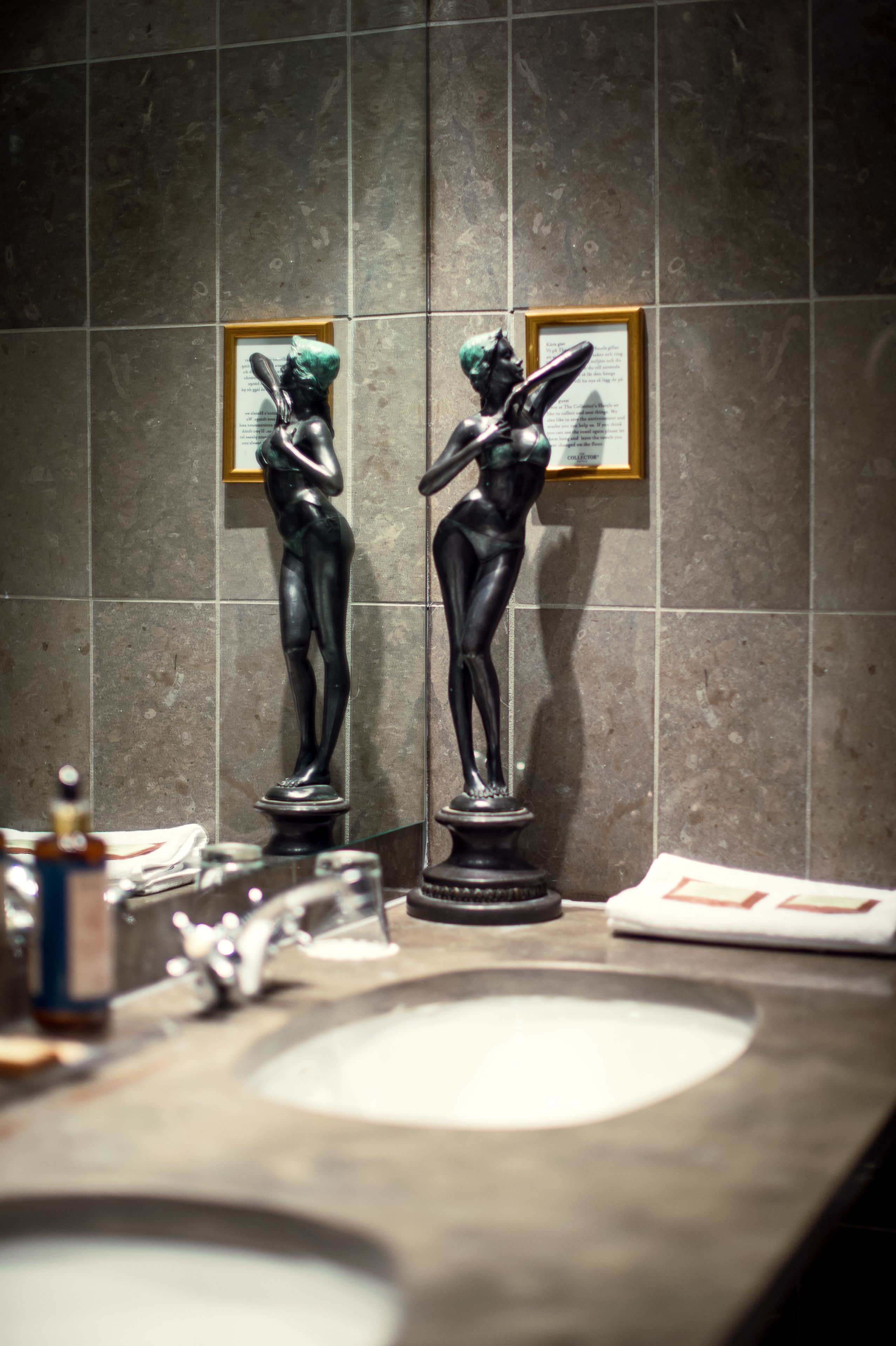Een badkamer met een wastafel, twee bronzen beeldjes en een ingelijst beeld aan de muur.
