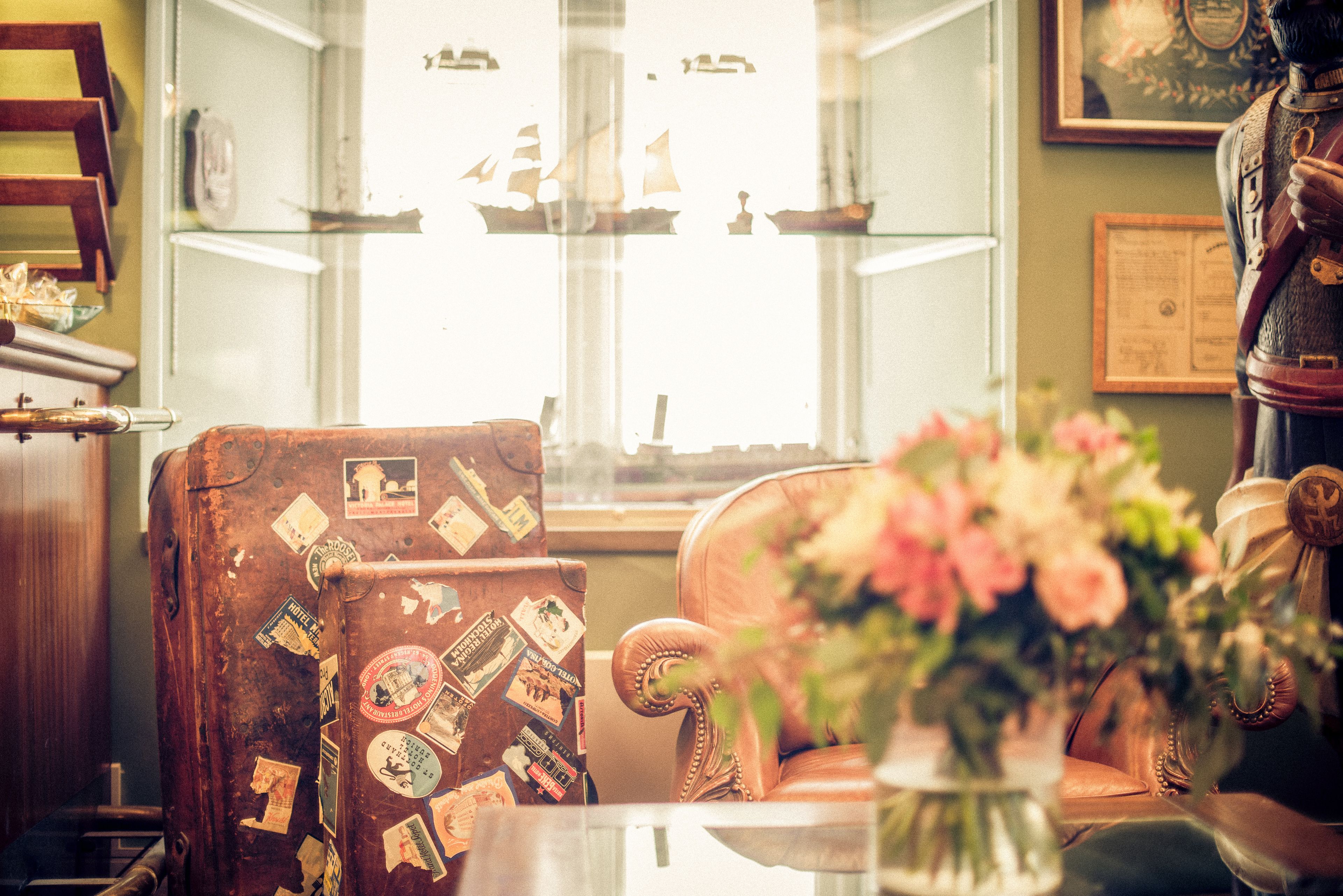 Una silla antigua con calcomanías de viajes, una vitrina de cristal con modelos de barcos y una estatua decorativa.