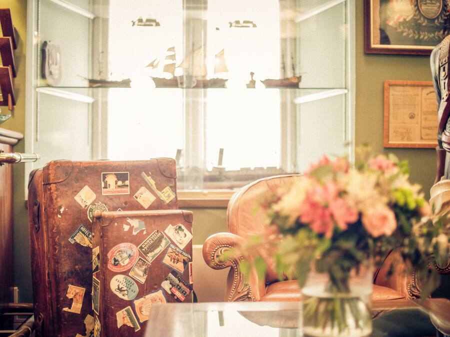 Una silla antigua con calcomanías de viajes, una vitrina de cristal con modelos de barcos y una estatua decorativa.