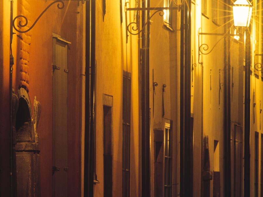 Una calle estrecha con farolas regularmente distribuidas y un edificio con puerta y ventana.