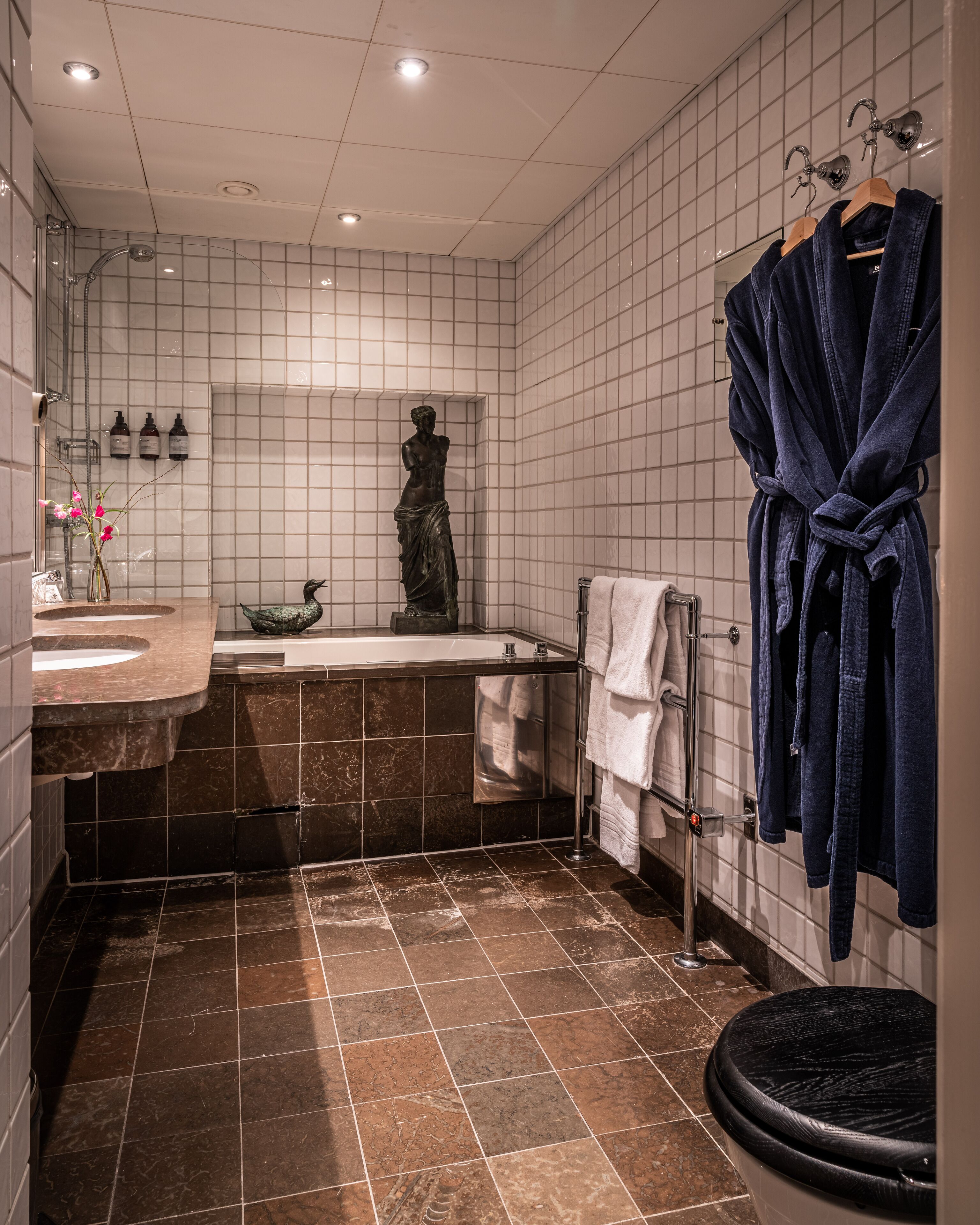 Et moderne badeværelse med en marmorvask, et fristående badekar og en statue.