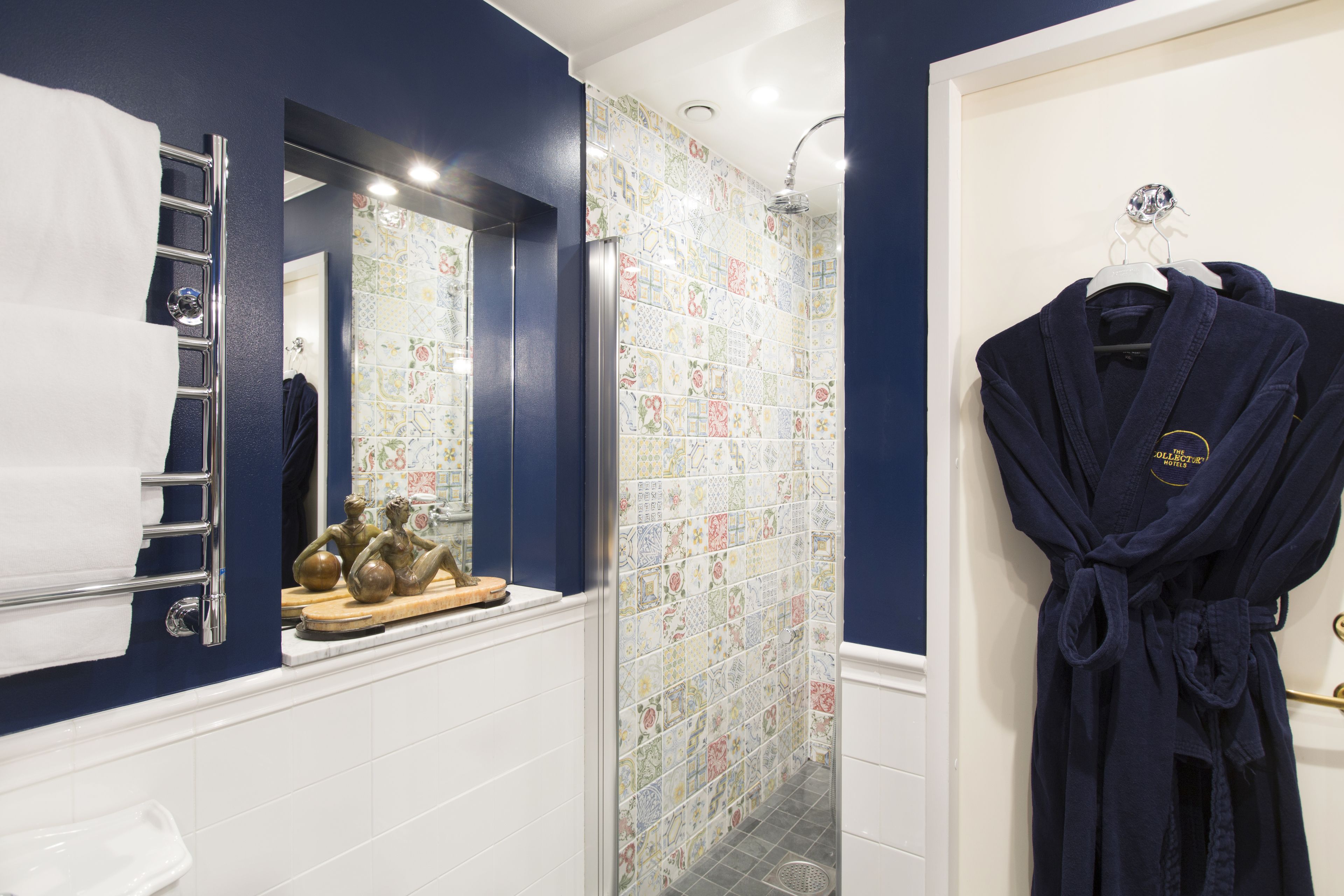 A bathroom with a blue wall, a shower with colorful tiles, a white sink, and a robe hanging on a rack.