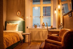 Un dormitorio acogedor con cama, escritorio y silla. Se ve una ventana con vistas al exterior, un radiador y un reloj en la pared.