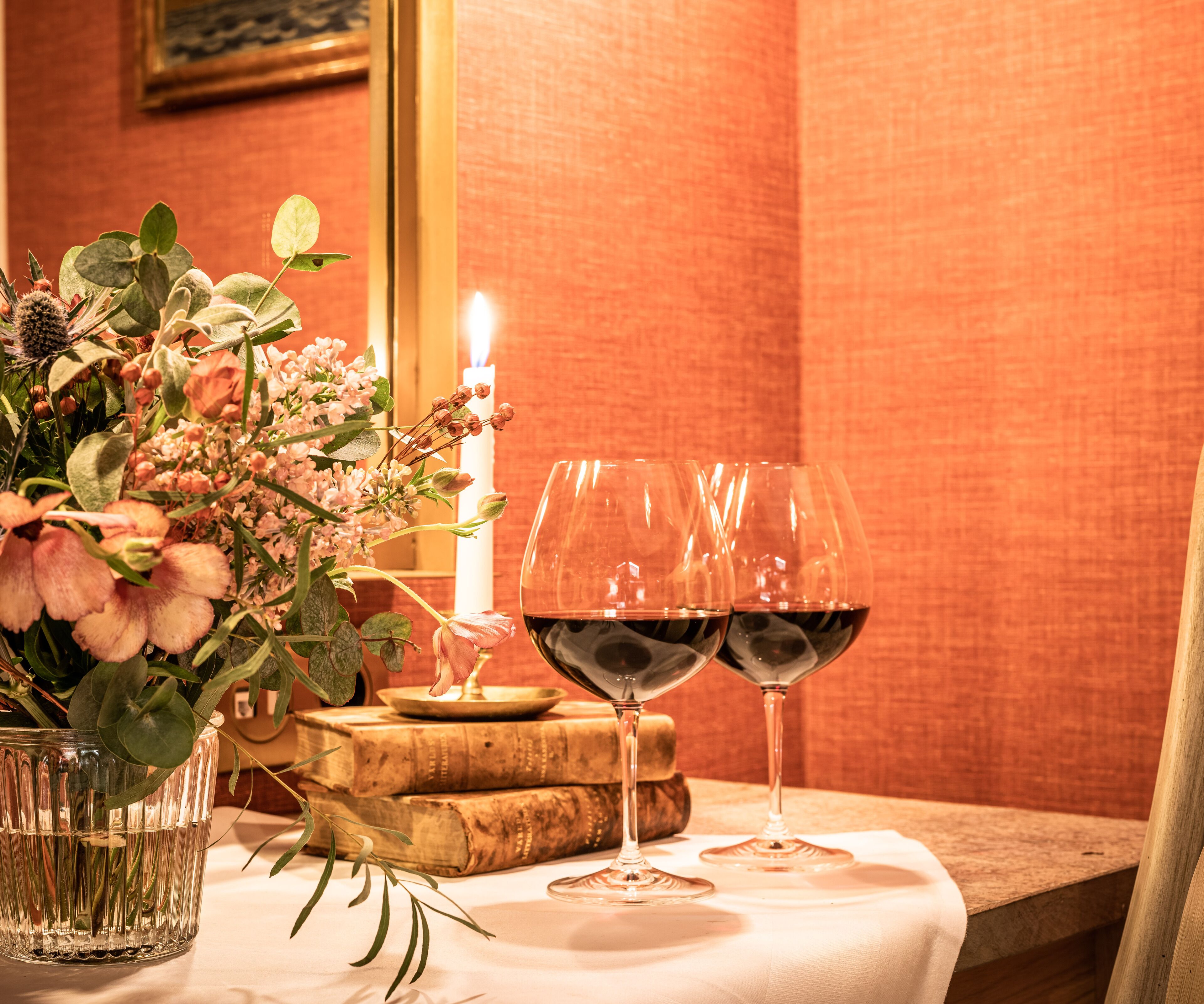 Una mesa con dos copas de vino, una vela y un florero con flores.