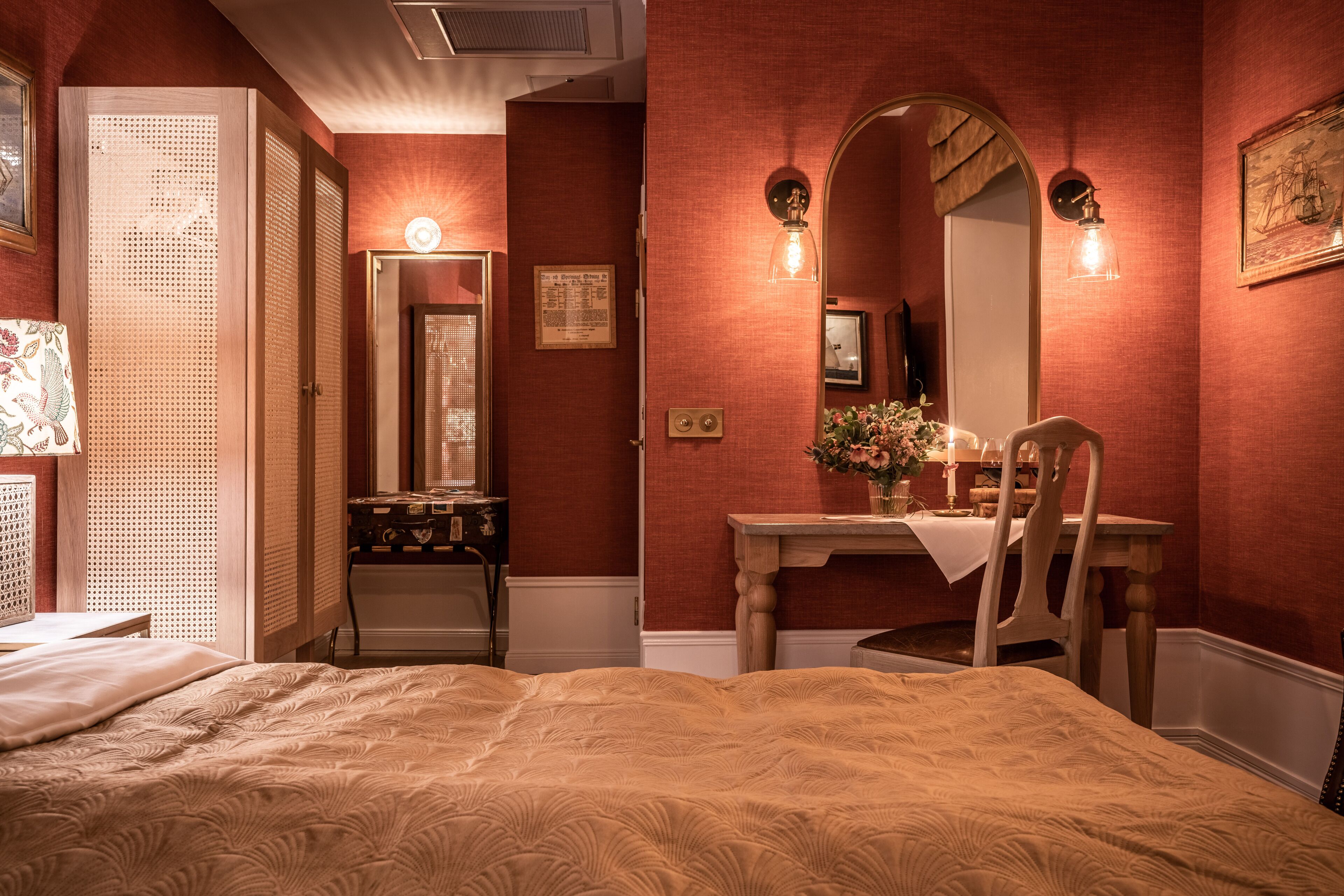Una habitación con cama, escritorio y silla, espejo, y lámpara de pared.