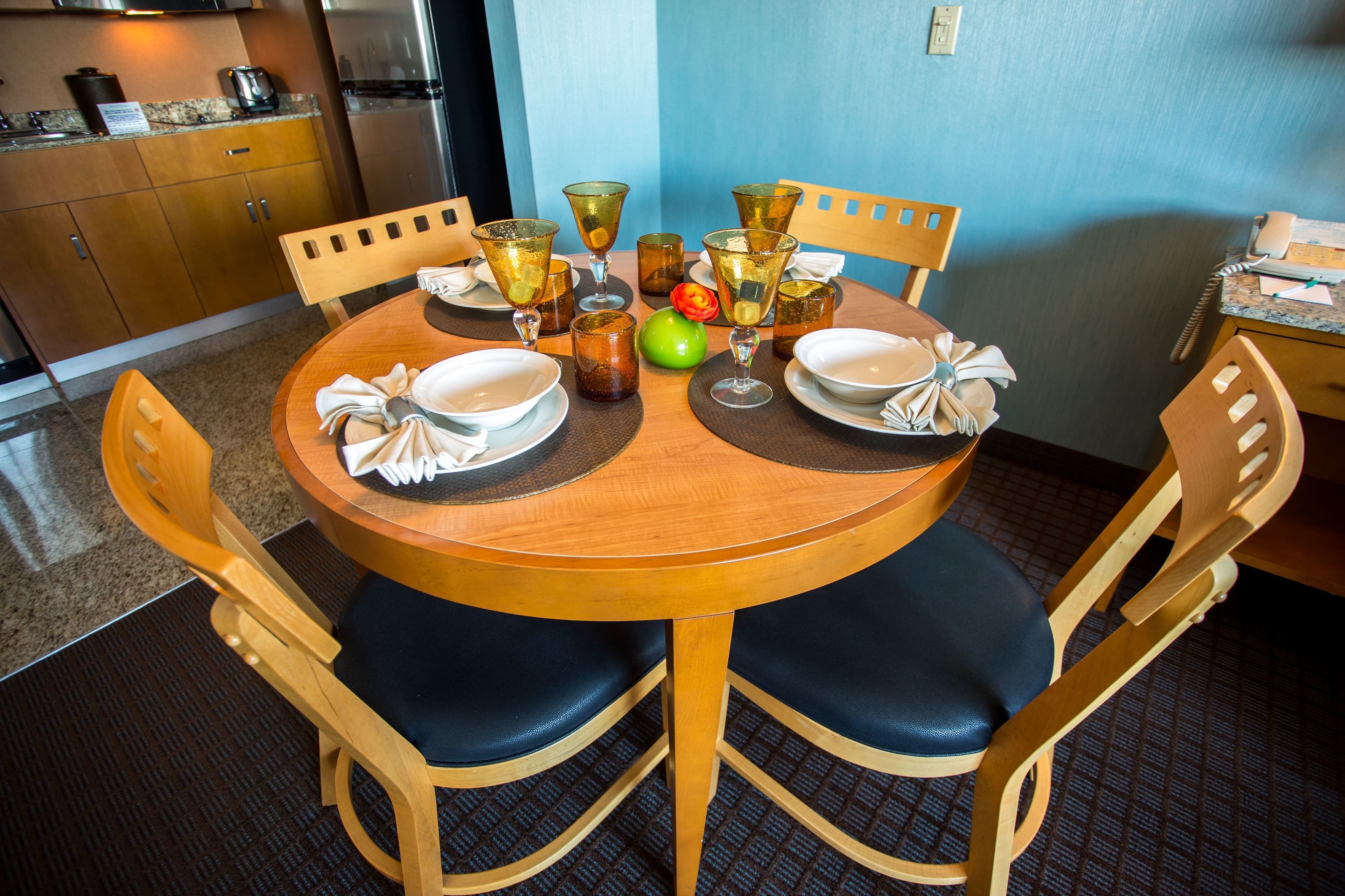A dining table with chairs, a kitchen in the background, and a blue wall.
