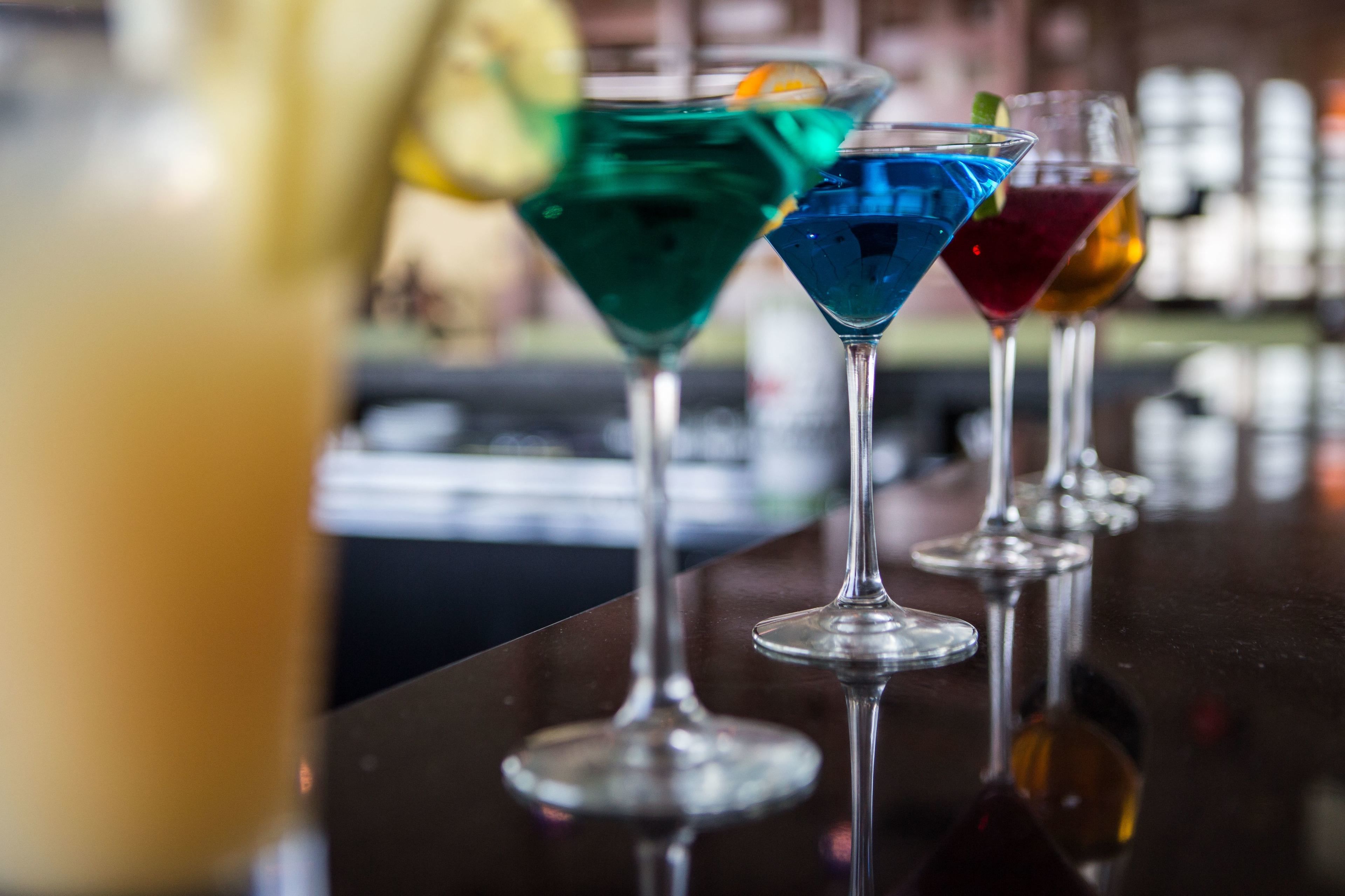 A row of colorful cocktails in martini glasses on a bar counter.