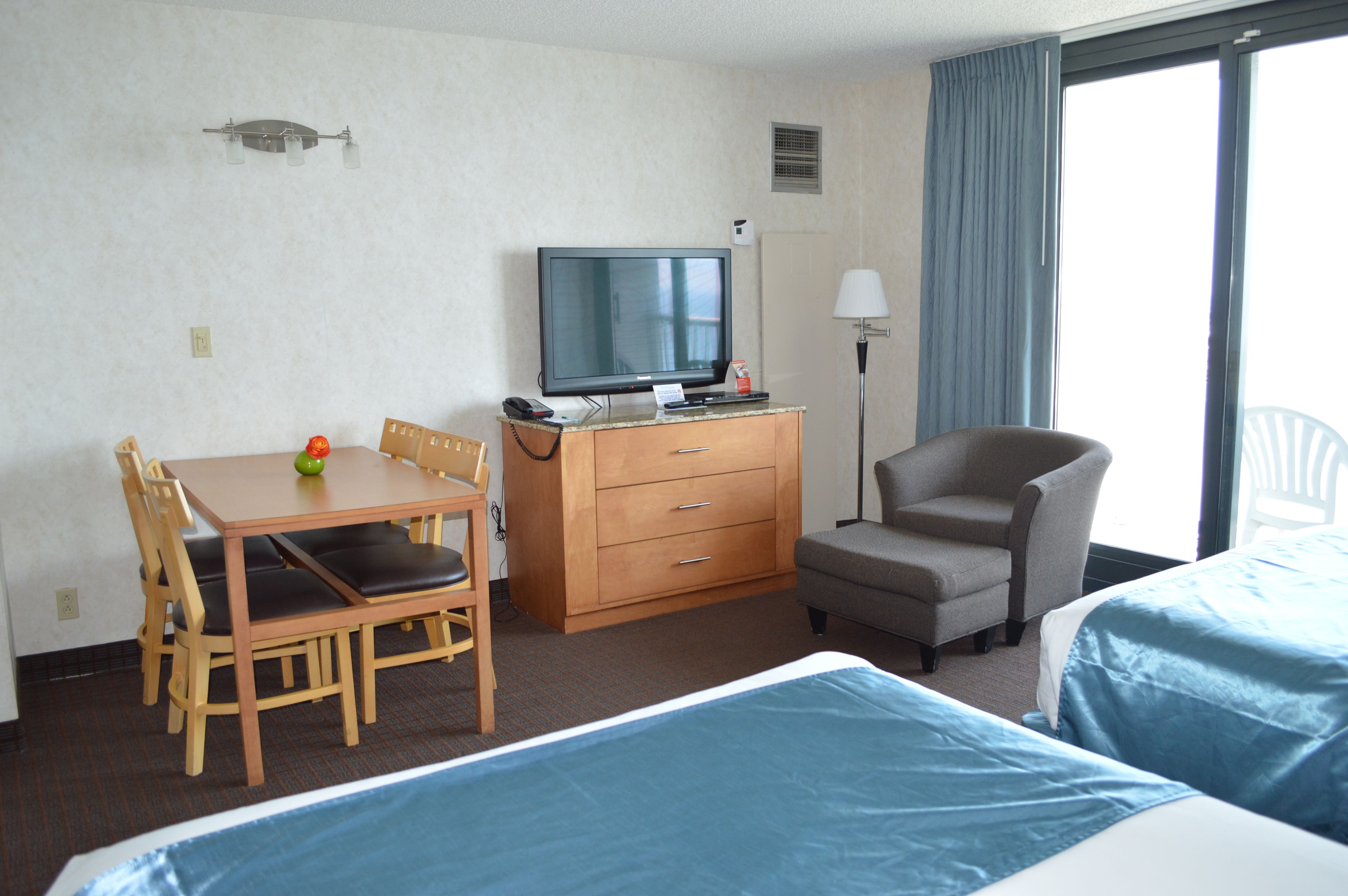 Ein Hotelzimmer mit einem Bett, einem Schreibtisch mit Computer, einem Sessel, einem Fernseher und einem Fenster mit Vorhängen.