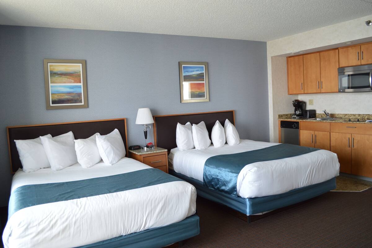 A hotel room with two beds, a kitchenette, and artwork on the walls.