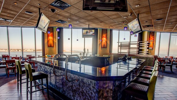 Zona de bar con una barra grande, diversas opciones de asientos y amplias ventanas con vistas a la ciudad.