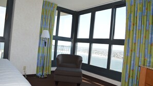 Una habitación de hotel con un ventanal grande, una cama, una silla y una lámpara.