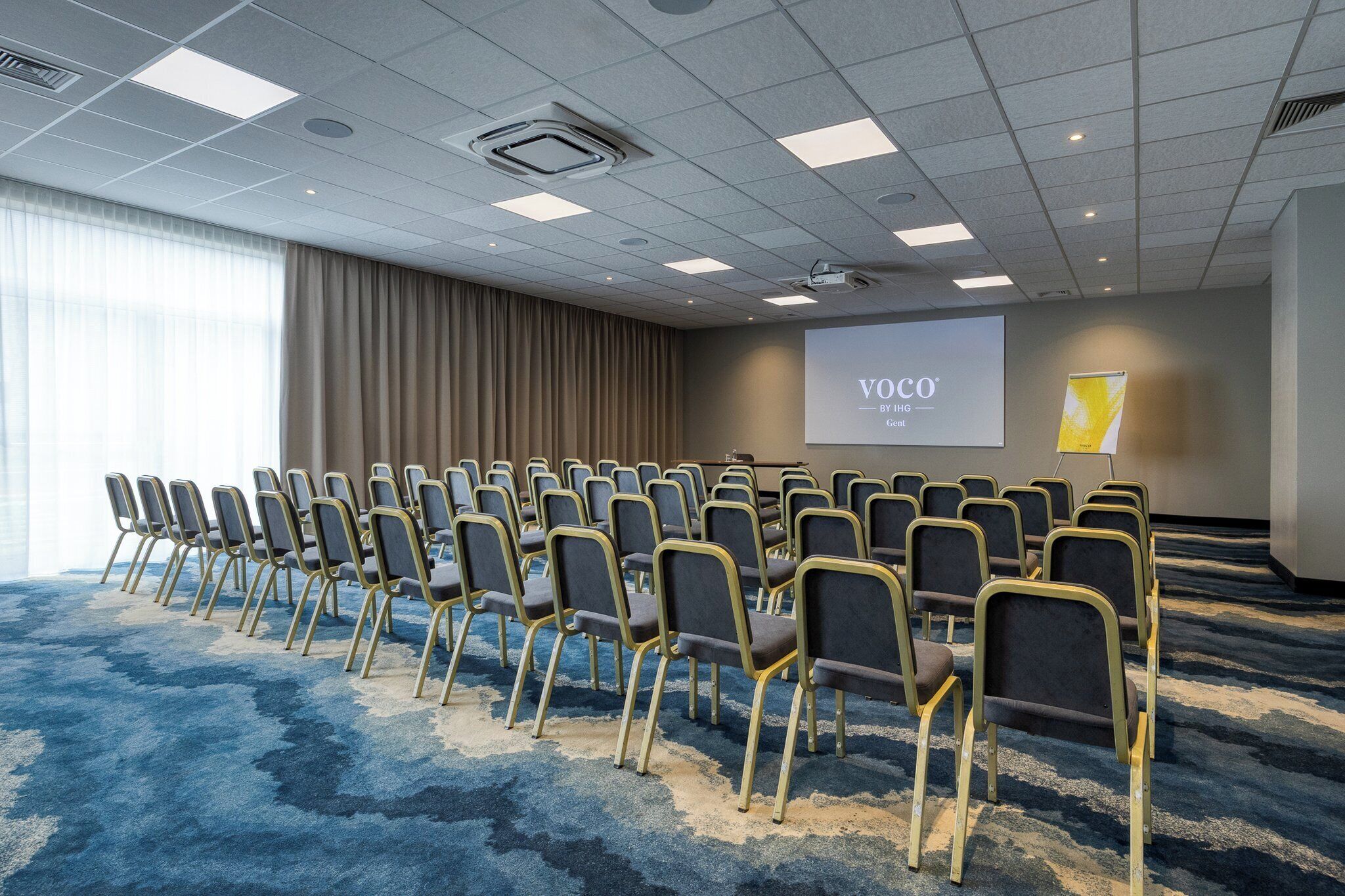 A conference room with rows of chairs, a projector screen, and a carpeted floor.