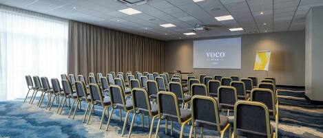 A conference room with rows of chairs, a projector screen, and a carpeted floor.