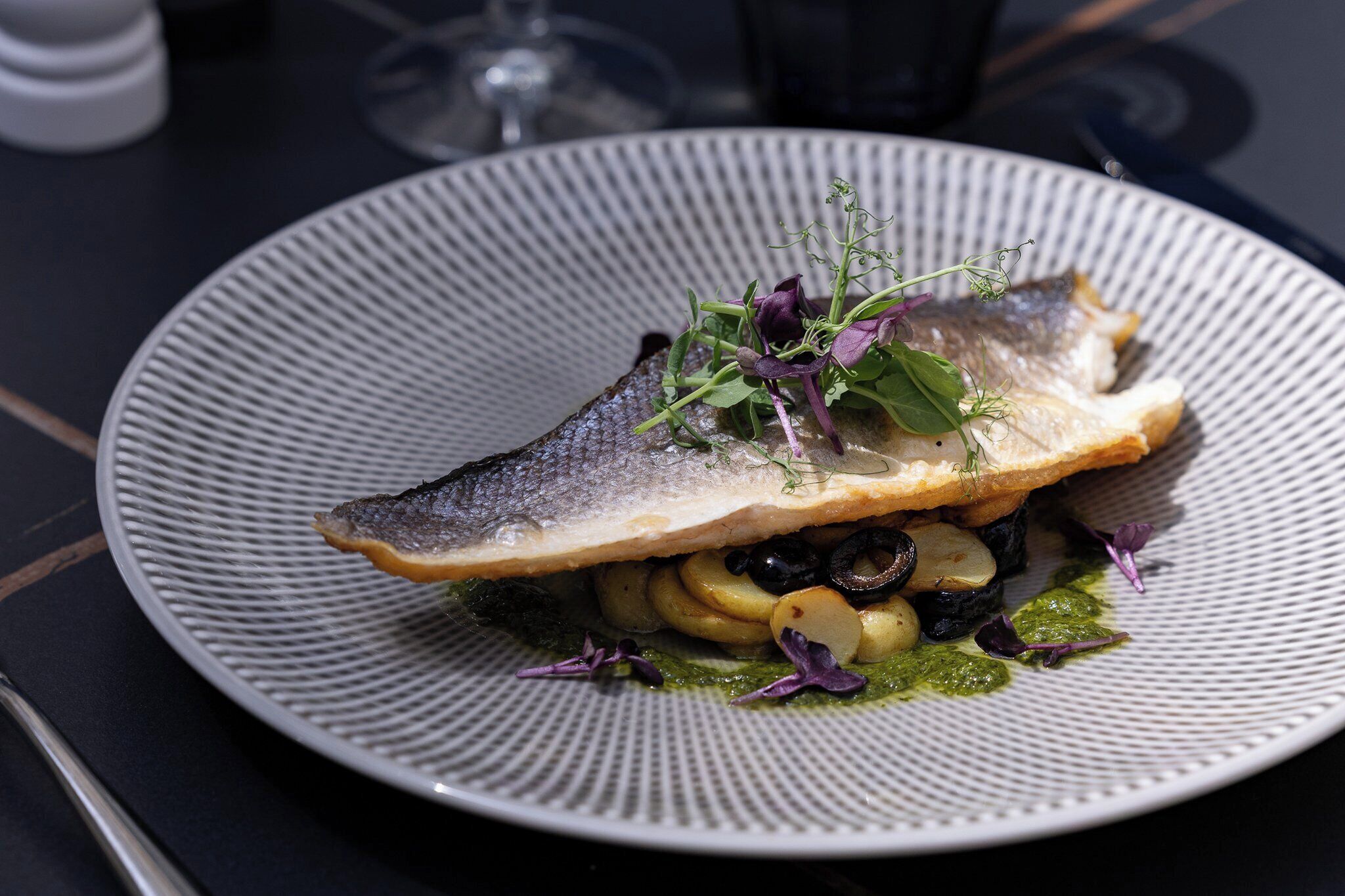 Un piatto con del pesce, verdure e salsa verde.