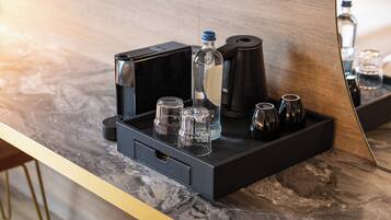 A hotel minibar with a coffee maker, a bottle, and several glasses on a marble countertop.