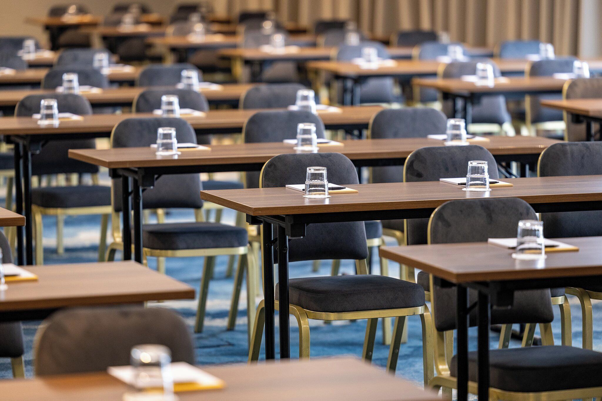 A conference room with rows of tables and chairs, each with a glass of water and a notepad.
