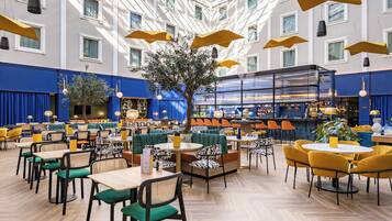 Un vaste espace de restauration intérieur offrant de nombreuses options de sièges, notamment des tables et des banquettes, ainsi qu’un arbre central qui apporte une touche naturelle.