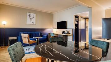 Una habitació d'hotel moderna amb una taula rodona de marbre negre, seients amb tapisseria blava i marró, un televisor de pantalla plana i una obra d'art emmarcada a la paret.