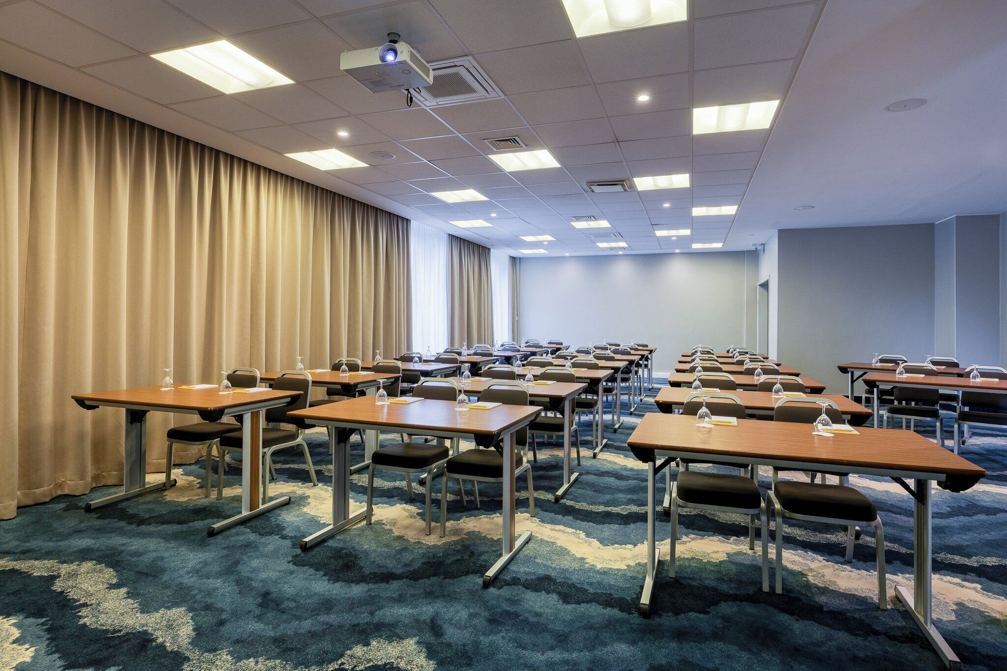 A conference room with multiple tables and chairs, a projector, and curtains.