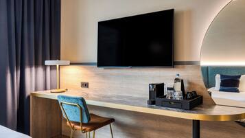 Hotelkamer met een flatscreen televisie aan de muur, een bureau met stoel, een nachtkastje met lamp en een bed met hoofdeinde.
