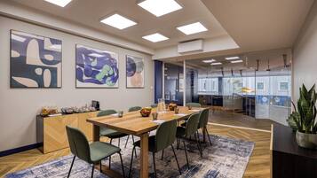 A modern office space with a wooden table, green chairs, abstract art on the wall, and a view into another room.