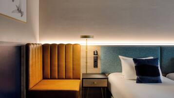 A hotel room with a bed, a nightstand, a lamp, a chair, and a wall-mounted shelf.