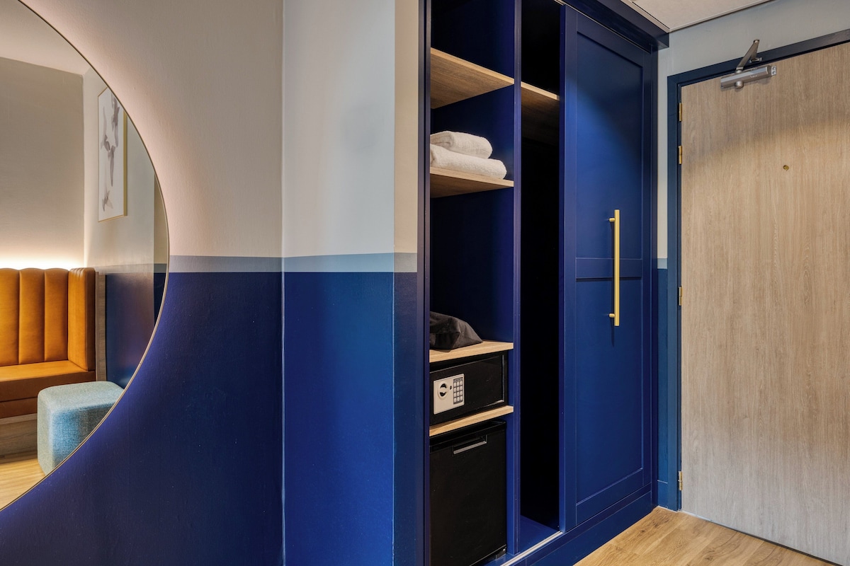A modern room with a curved wall, a wooden bench, a wardrobe with a blue door, and a small black appliance.