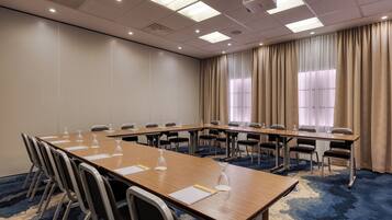 Un salón de conferencias con una larga mesa, sillas y un proyector.