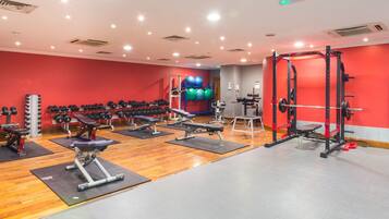 Un gimnasio con varios equipos de ejercicio, incluyendo mancuernas, bancos y una jaula para sentadillas.
