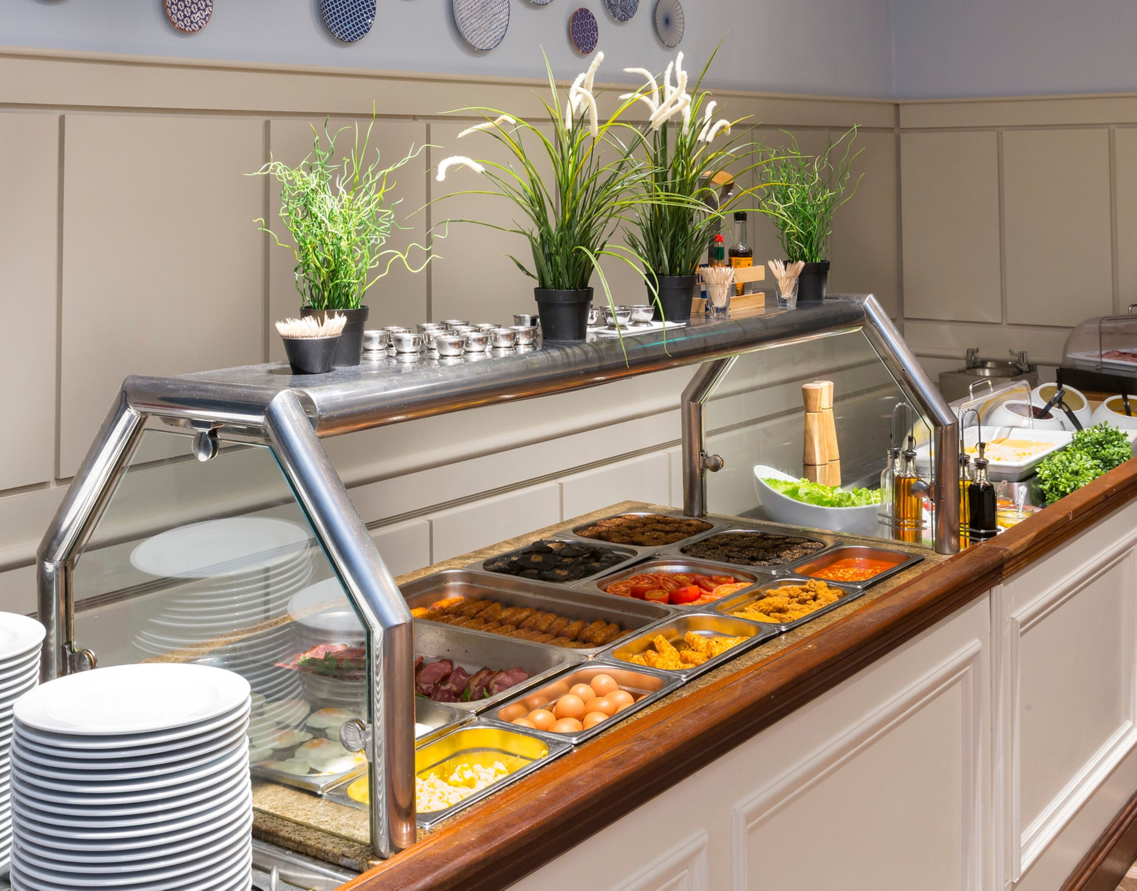 A buffet setup with various food items, including eggs, meats, and salads, in a buffet line with a glass barrier.