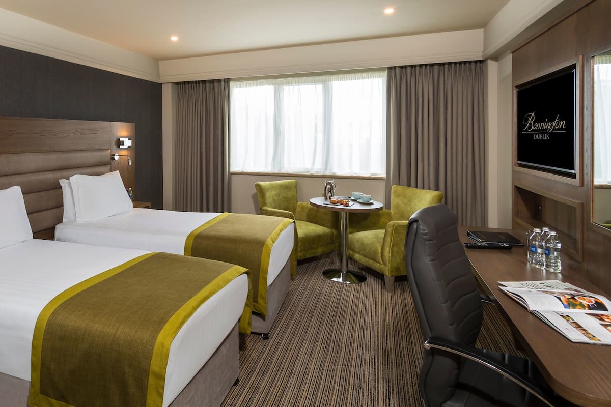 Ein Hotelzimmer mit zwei Betten, einem Schreibtisch mit Stuhl, einem kleinen Tisch und einem Fernseher.