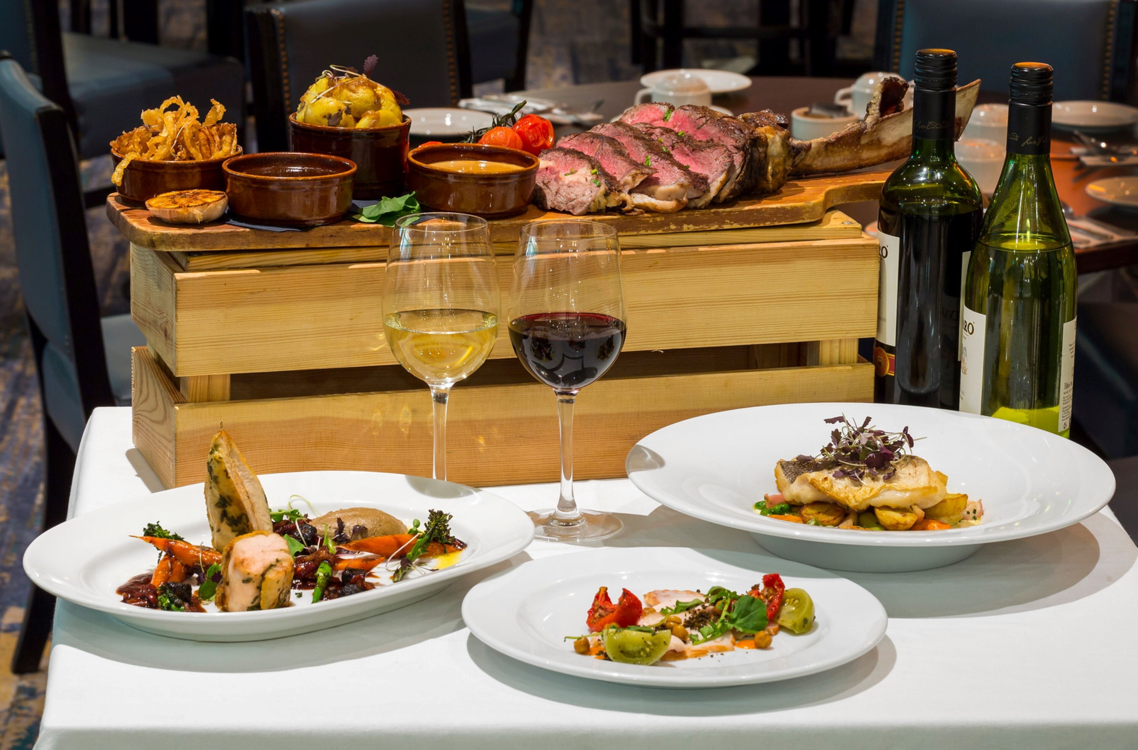 A dining table with various dishes, including a steak, seafood, and vegetables, along with wine bottles and glasses.