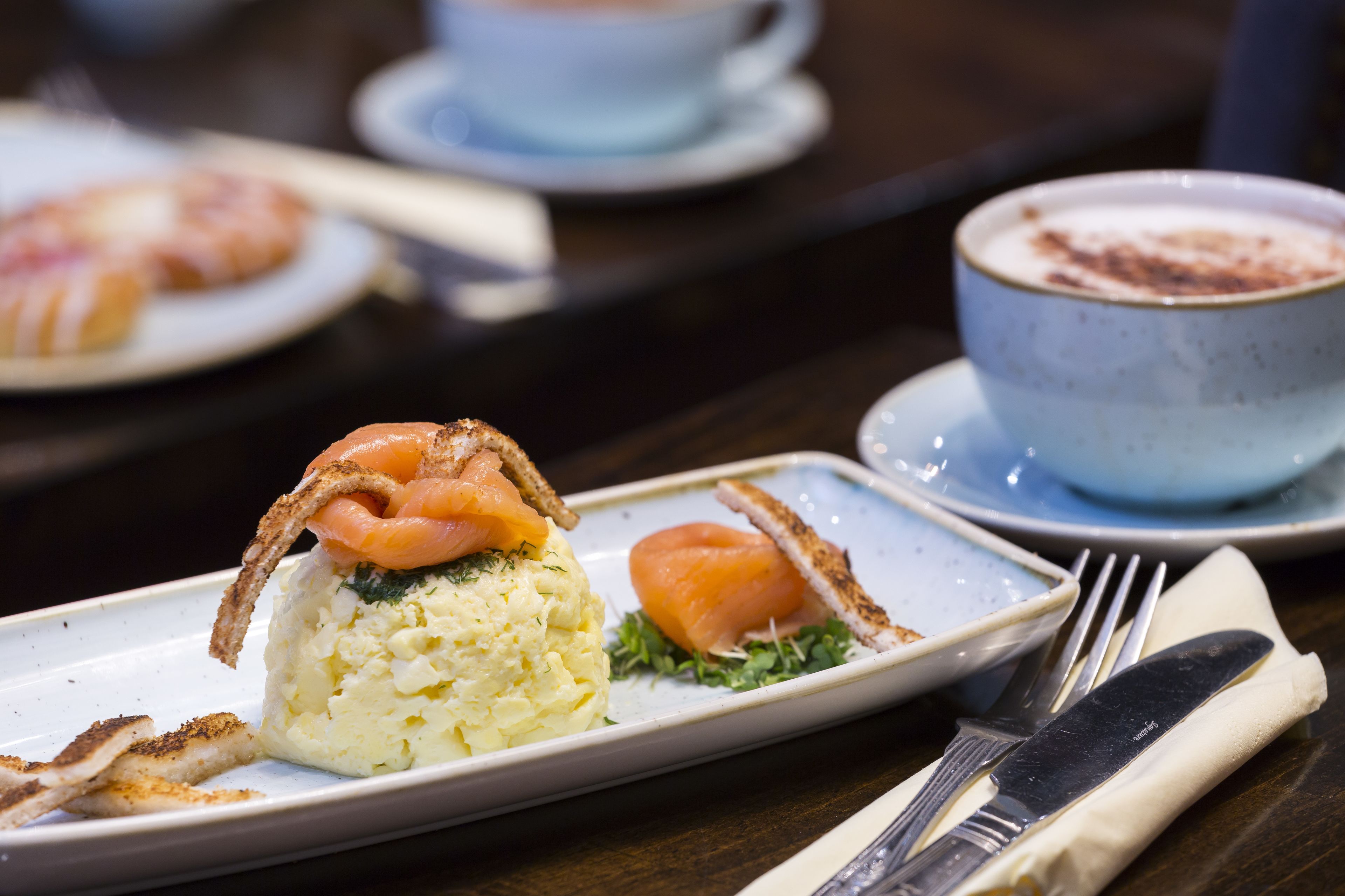A plate with a salmon dish, a cup of coffee, and a fork and knife on a table.