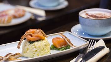 A plate with a salmon dish, a cup of coffee, and a fork and knife on a table.