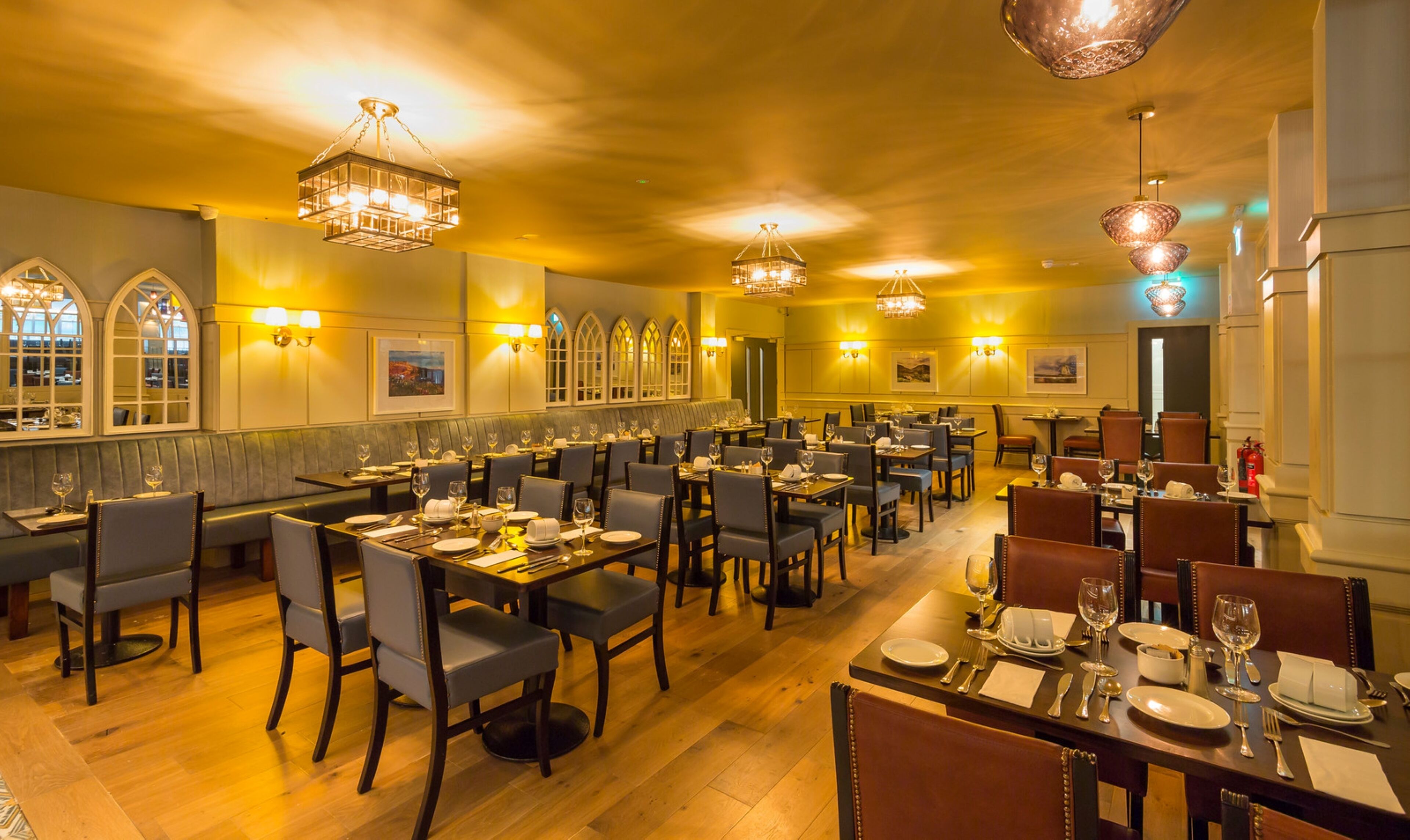 A restaurant with multiple dining tables and chairs, warm lighting, and large windows with decorative frames.