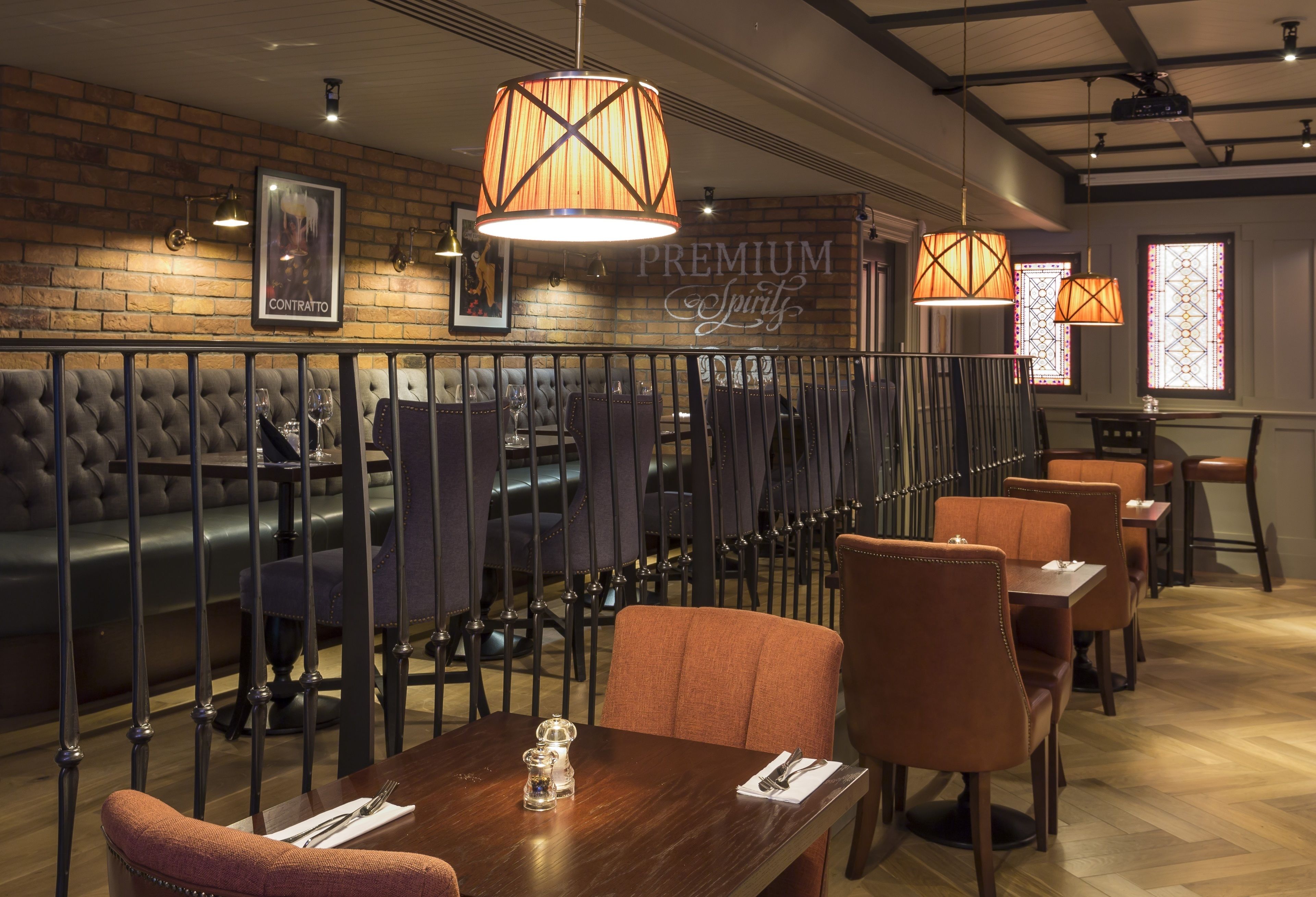 A restaurant interior with a brick wall, cushioned seating, and pendant lighting.