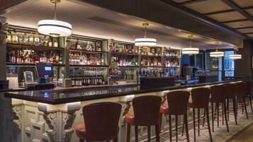 A bar area with a long counter, multiple shelves of liquor bottles, and several bar stools.